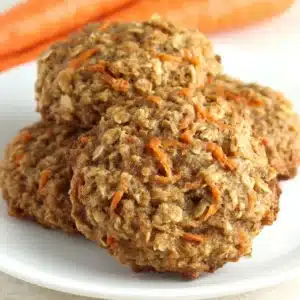 Freshly baked carrot cake oatmeal cookies on white plate with visible carrot shreds