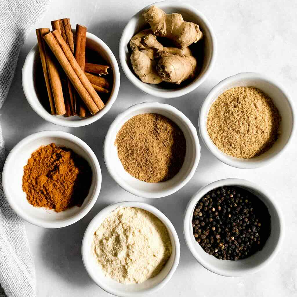 Pumpkin pie spice ingredients in white bowls including cinnamon, ginger, and nutmeg
